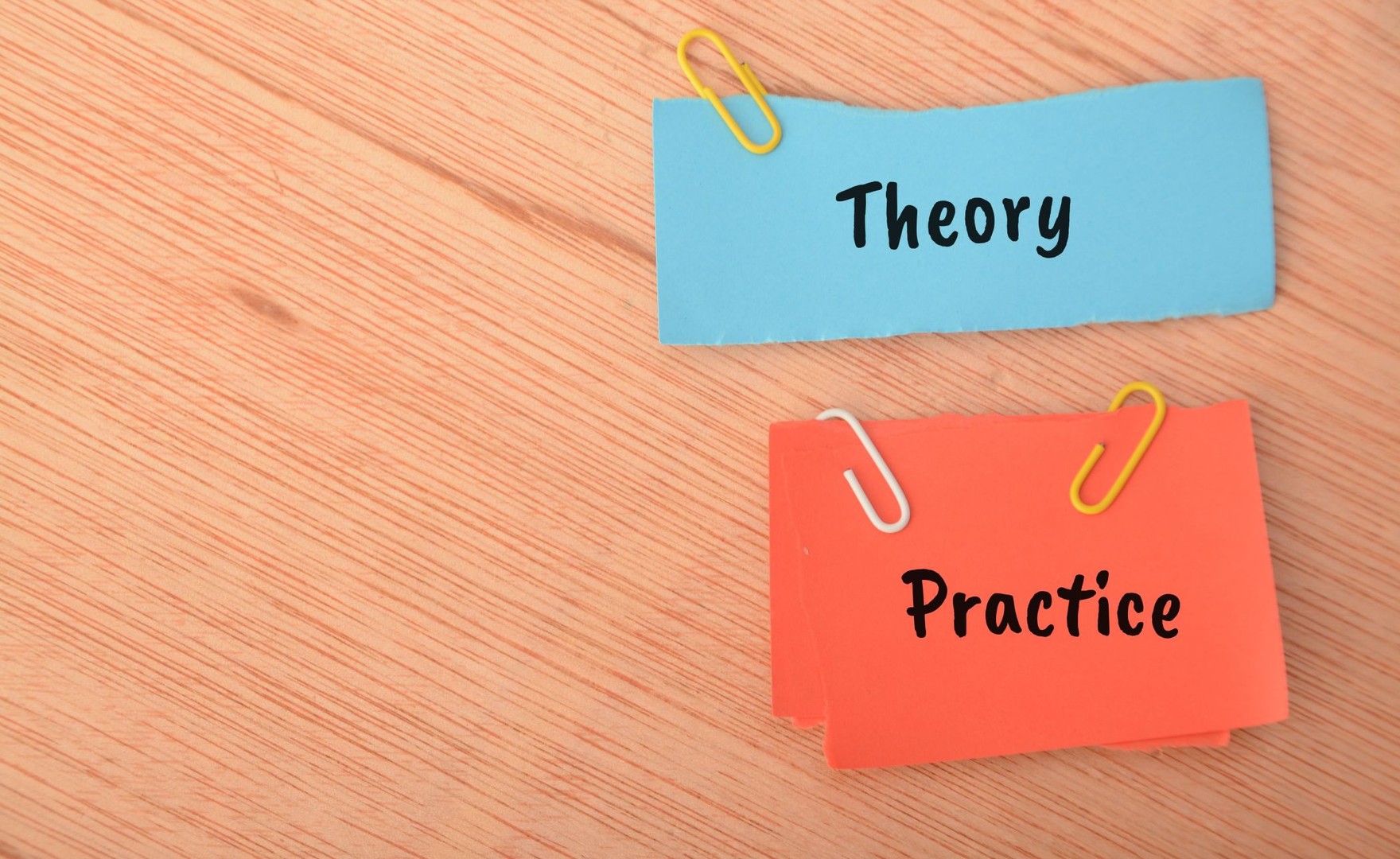 Two pieces of card on a table reading 'theory' and 'practice'