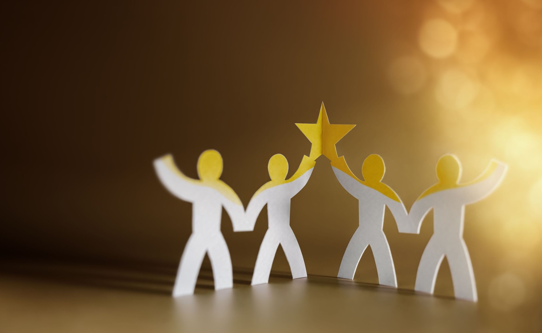 Four paper cut-outs of figures holding up a star