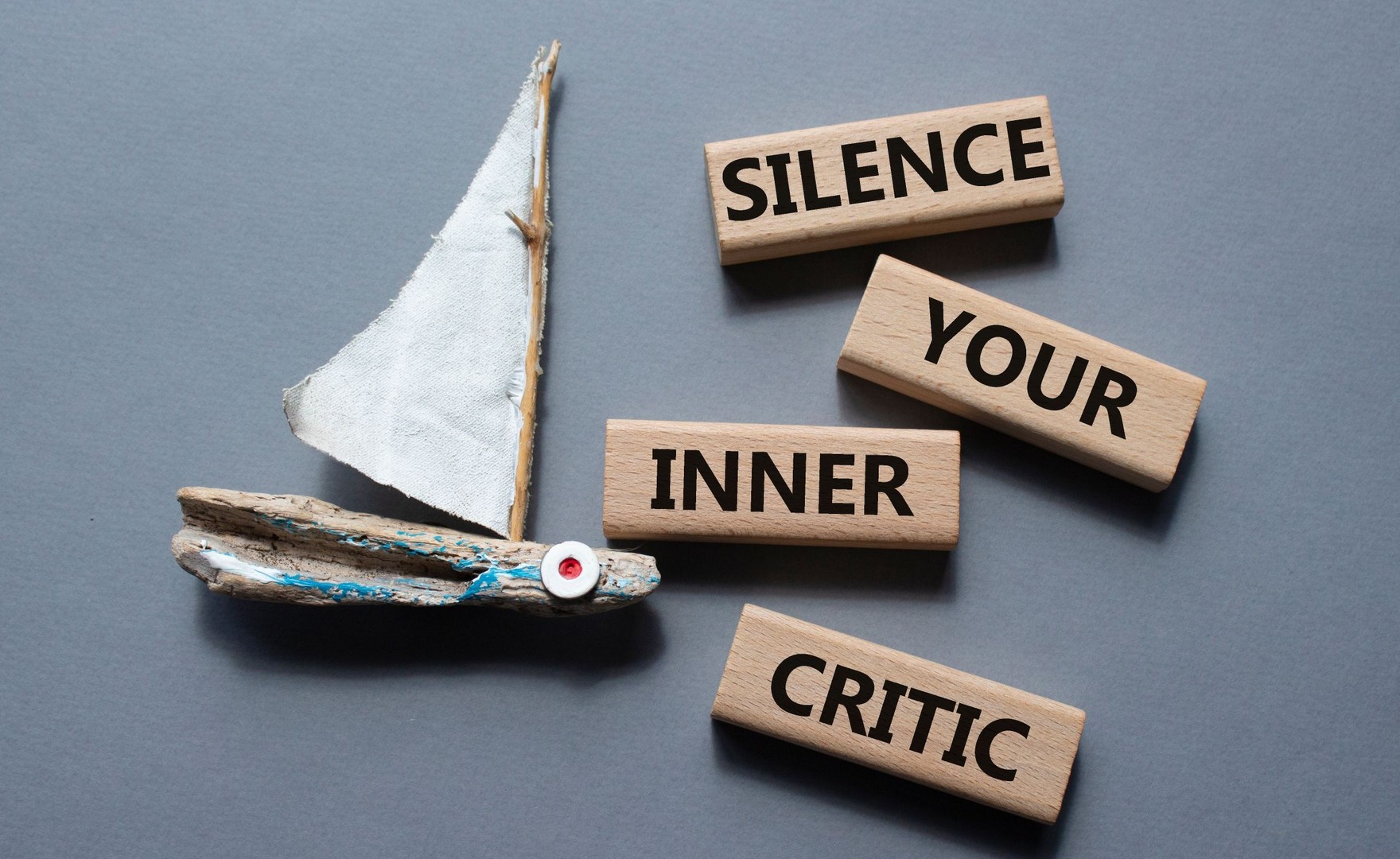 small, wooden toy boat next to words 'silence your inner critic'